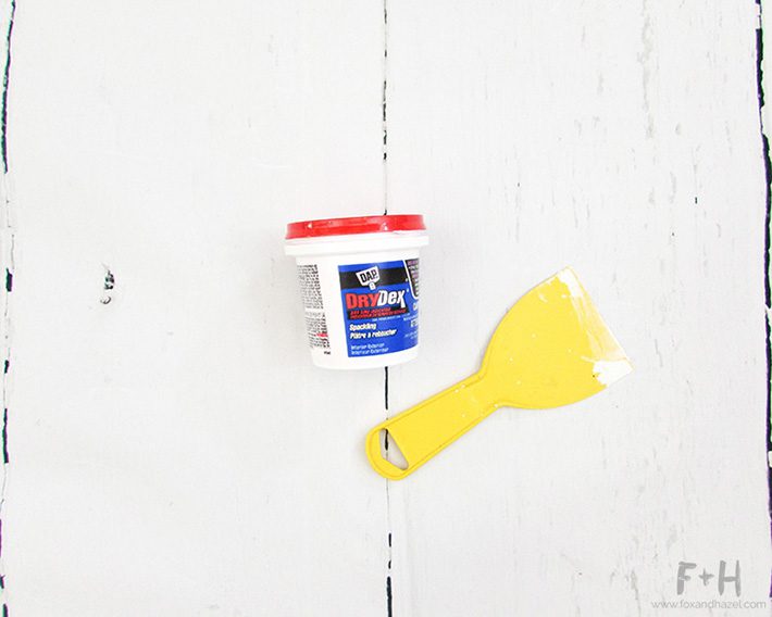 small tub of drywall compound and yellow plastic spackling tool on white background