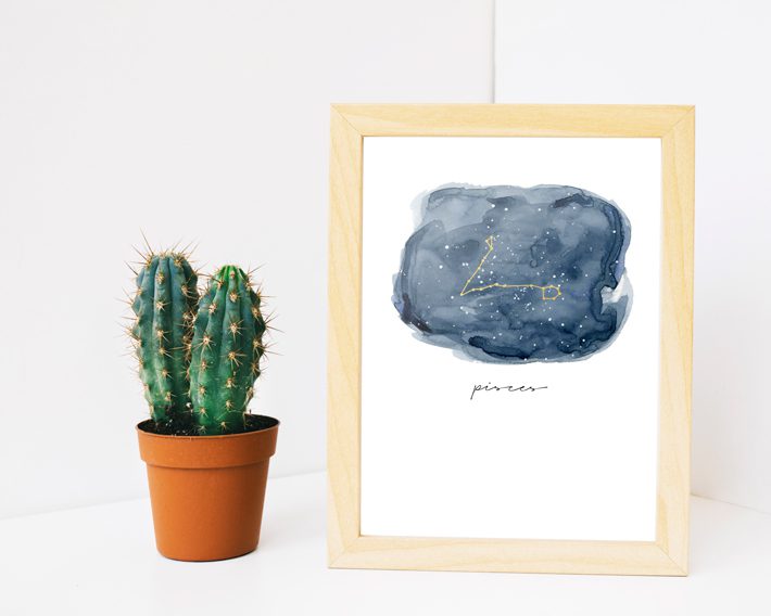 zodiac sign art in wood frame next to cactus on white background