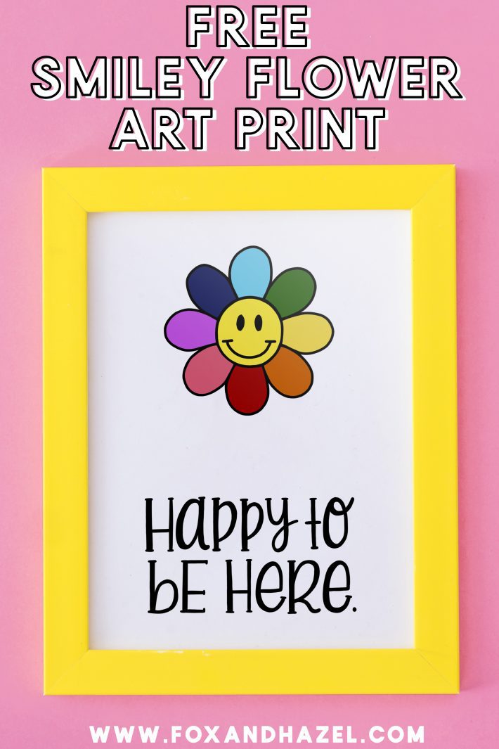 free smiley flower art print in yellow frame with words "happy to be here" on a pink background