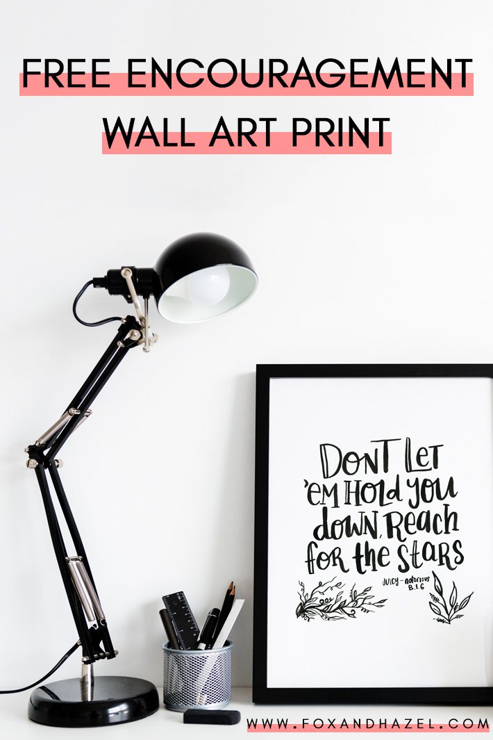 encouragement wall art print in black frame on desk next to black desk lamp and office supplies.