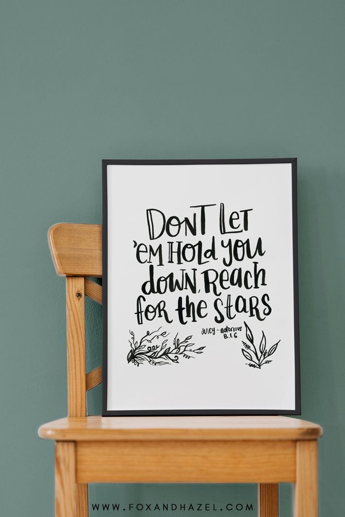 notorious B.I.G lyrics handlettered on poster in black frame, sitting on a wooden chair against a green wall