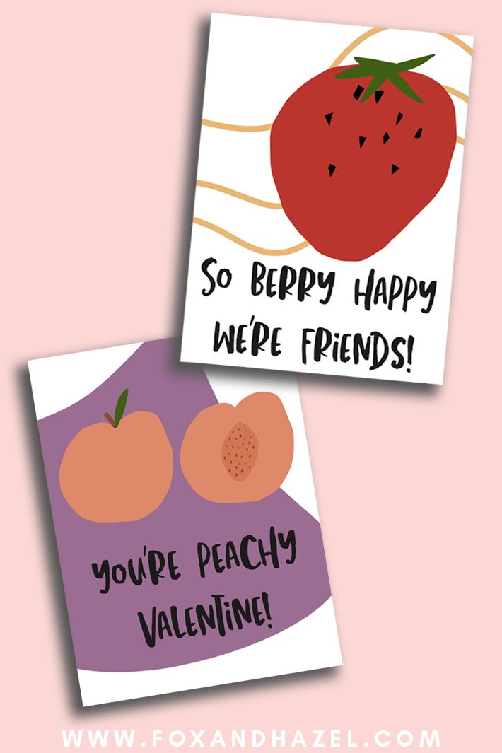 Two fruit Valentine's Day cards lay on a pink background. One card has a strawberry and reads "So berry happy we're friends". The second card has peaches and reads "You're peachy, Valentine!"